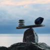 A stacked stone scale at the edge of a mountainous body of water represents balancing founder-led company needs after a private equity transition