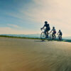 Three people pedaling bicycles are leading a road cycling race through a valley with tree-covered hillsides in the distance. The image also shows the forward motion and a blur from the speed at which the cyclists are traveling. The image symbolizes PE-backed leadership requiring a different approach and pace.