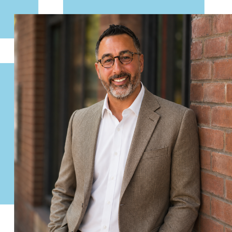 Tony_Gerbino_Bio_Page_CORRECT_SIZE Tony Gerbino headshot. Tony stands against a wall in an outdoor backdrop in a suit jacket and smiles.